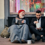 Illustration d’une main tendue entourée d’icônes numériques de crowdfunding, symbolisant la privatisation de la compassion et le marché de la vulnérabilité.