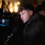 Portrait de Raphaël Arnault en situation publique, debout ou en déplacement, dans un cadre urbain ou institutionnel. L’image évoque son engagement antifasciste, son parcours militant et son rôle de député, dans une atmosphère sobre et journalistique.