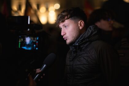 Portrait de Raphaël Arnault en situation publique, debout ou en déplacement, dans un cadre urbain ou institutionnel. L’image évoque son engagement antifasciste, son parcours militant et son rôle de député, dans une atmosphère sobre et journalistique.