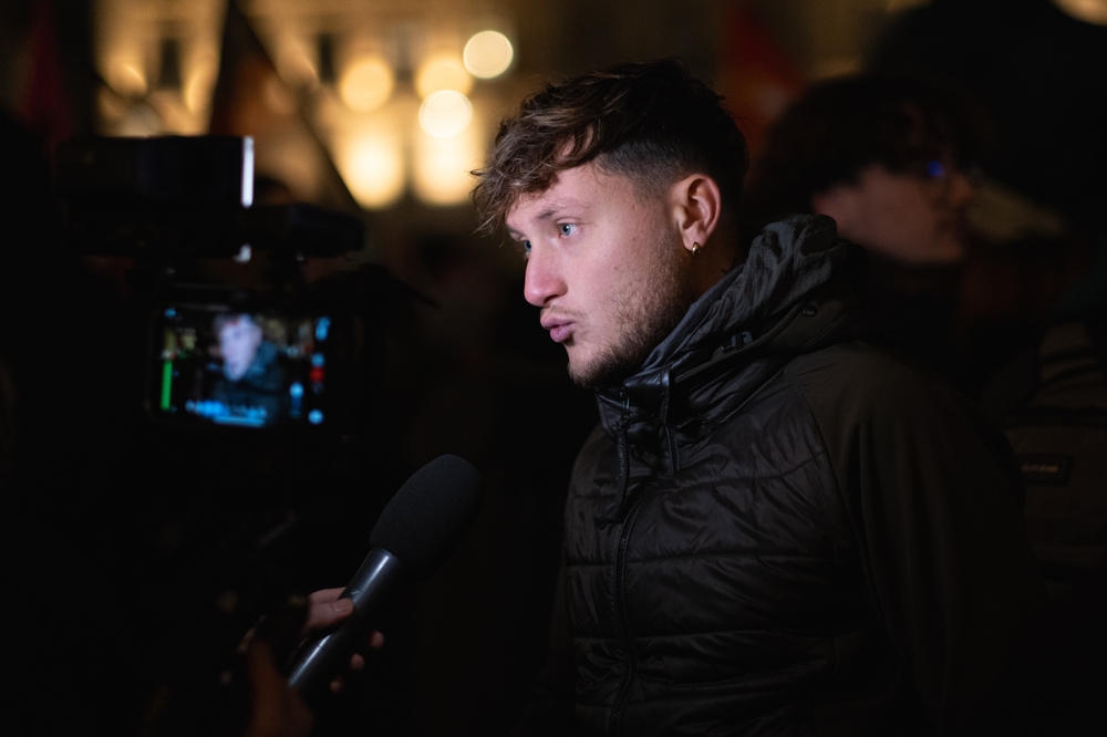 Portrait de Raphaël Arnault en situation publique, debout ou en déplacement, dans un cadre urbain ou institutionnel. L’image évoque son engagement antifasciste, son parcours militant et son rôle de député, dans une atmosphère sobre et journalistique.