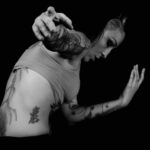 Mélanie Paolettoni accompagne un patient dans un mouvement doux et guidé, dans une salle lumineuse et épurée. Son attitude est attentive et bienveillante, les gestes sont lents et fluides, exprimant écoute du corps, confiance retrouvée et apaisement. L’ambiance est chaleureuse, centrée sur la relation et la présence.