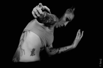 Mélanie Paolettoni accompagne un patient dans un mouvement doux et guidé, dans une salle lumineuse et épurée. Son attitude est attentive et bienveillante, les gestes sont lents et fluides, exprimant écoute du corps, confiance retrouvée et apaisement. L’ambiance est chaleureuse, centrée sur la relation et la présence.