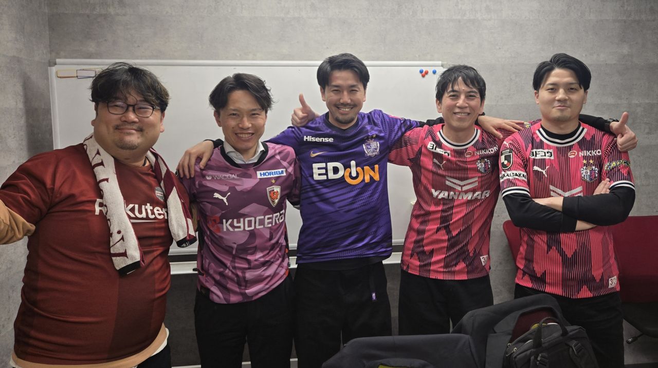 Photo de supporters réunis autour d’un écran diffusant un match de J‑League, partageant repas et analyses dans une ambiance conviviale.