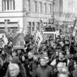 Une silhouette de l’hémicycle vue en plongée, traversée par une fissure lumineuse qui sépare symboliquement les blocs politiques. L’atmosphère est crépusculaire, évoquant la fin d’un cycle républicain et la recomposition des frontières du légitime.