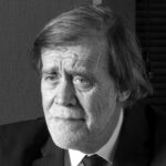 Jean‑Pierre Servel, assis dans son bureau à Carqueiranne, entouré de sa bibliothèque de livres anciens, regard bleu et expression concentrée.