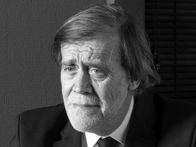 Jean‑Pierre Servel, assis dans son bureau à Carqueiranne, entouré de sa bibliothèque de livres anciens, regard bleu et expression concentrée.