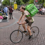 Livreurs Uber Eats et Deliveroo circulant en ville, illustrant la plainte déposée pour traite d’êtres humains et les conditions de travail dénoncées.