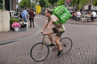 Livreurs Uber Eats et Deliveroo circulant en ville, illustrant la plainte déposée pour traite d’êtres humains et les conditions de travail dénoncées.