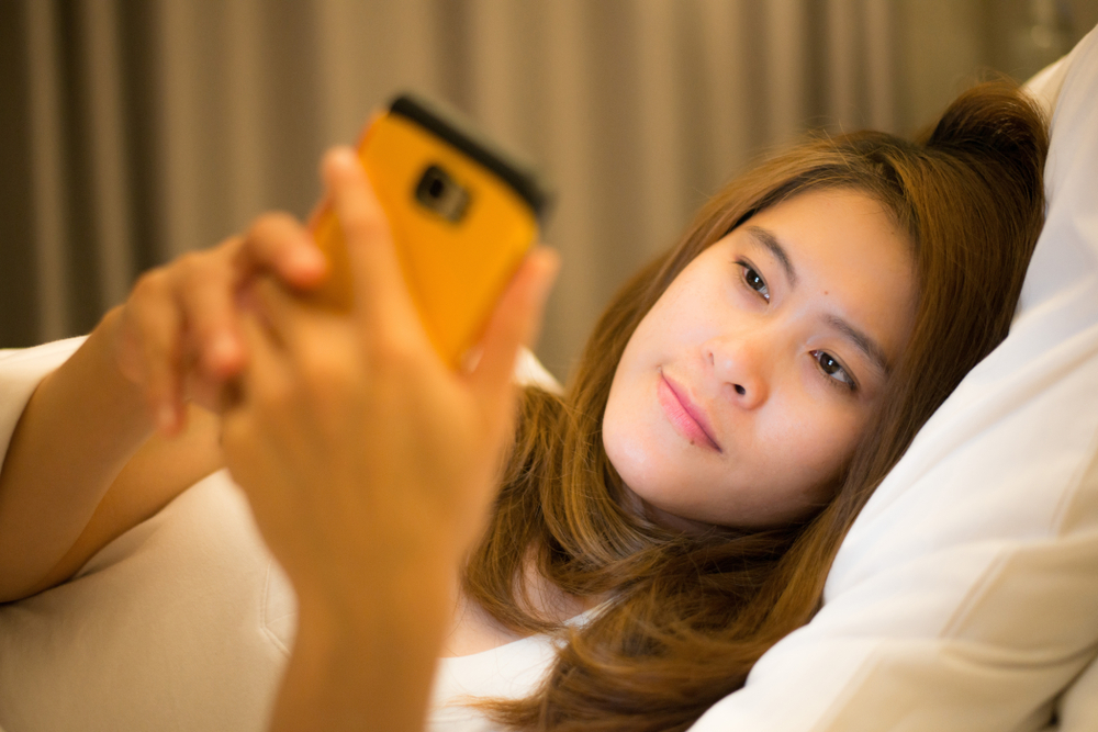Jeune adulte absorbé par son smartphone, illustrant la dépendance aux réseaux sociaux et ses implications sociales.