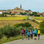 Une famille avançant sur un sentier du chemin de Saint‑Jacques, au milieu de paysages vallonnés baignés de lumière, symbolisant le voyage, la lenteur et le partage intergénérationnel.