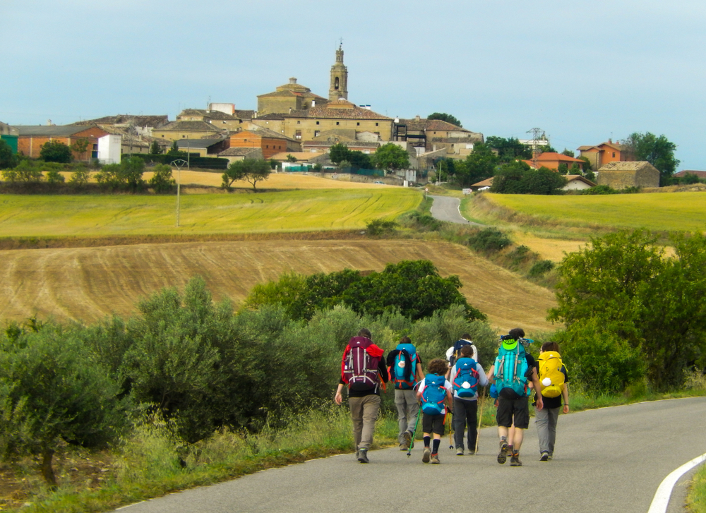 Une famille avançant sur un sentier du chemin de Saint‑Jacques, au milieu de paysages vallonnés baignés de lumière, symbolisant le voyage, la lenteur et le partage intergénérationnel.