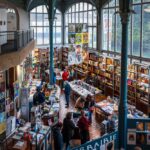 Une librairie indépendante animée, avec des lecteurs parcourant les rayons et un libraire en discussion avec ses clients.