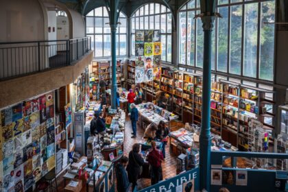 Une librairie indépendante animée, avec des lecteurs parcourant les rayons et un libraire en discussion avec ses clients.